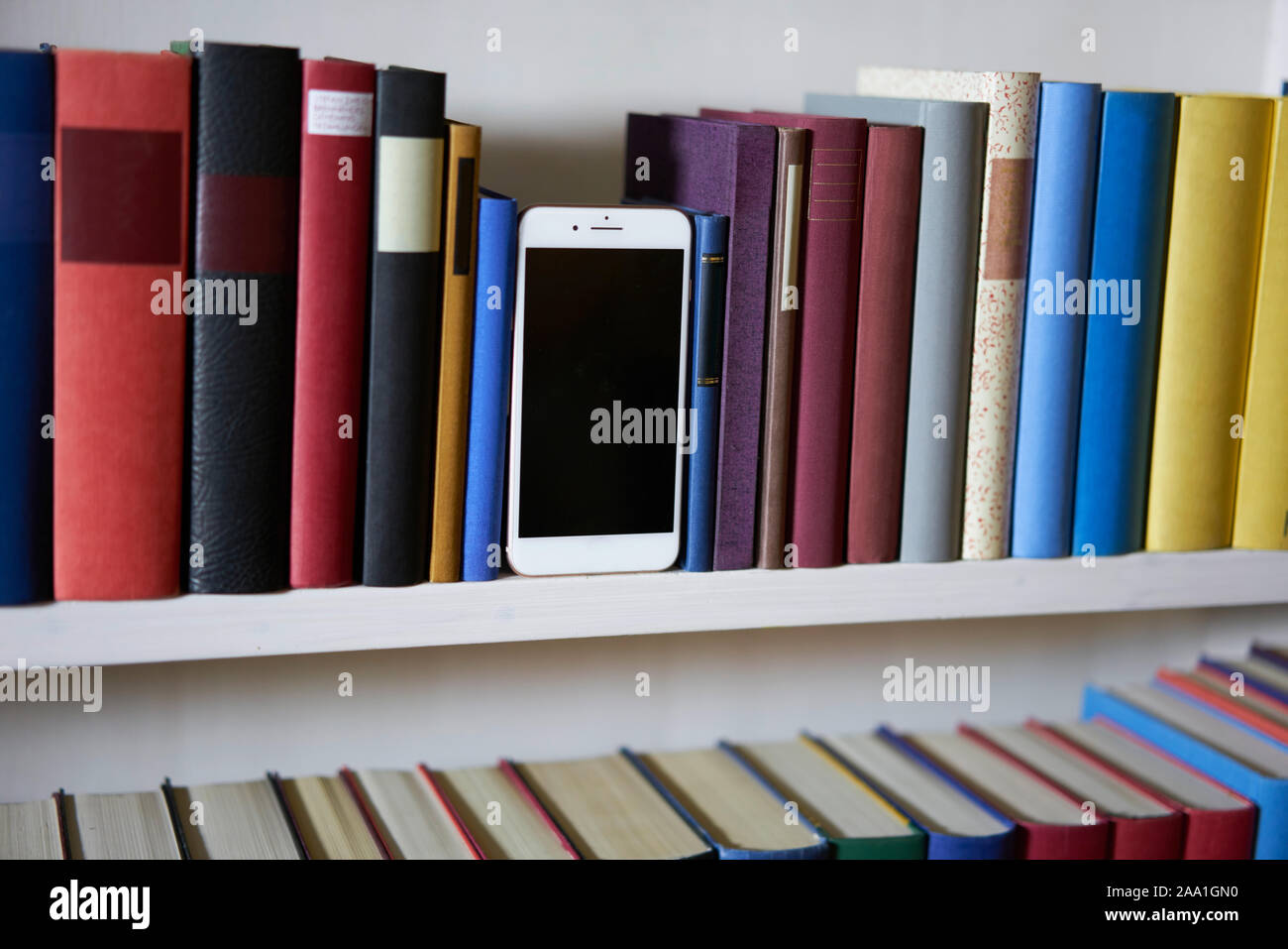 Mobile phone in colorful and accurate bookshelf, standing upright Stock Photo