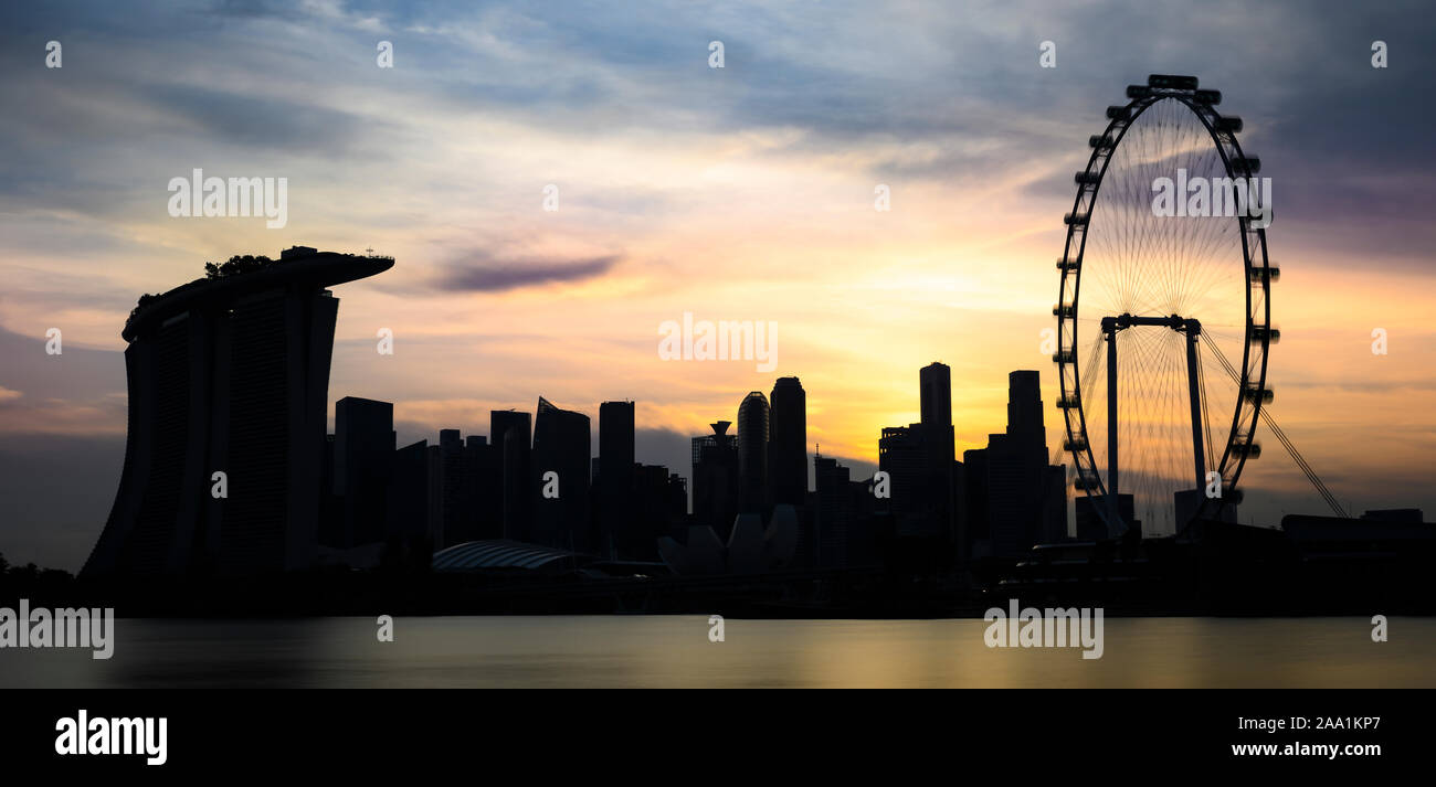 Stunning view of the silhouette of the Marina Bay skyline with skyscrapers and a ferry wheel during a breathtaking sunset in Singapore. Stock Photo