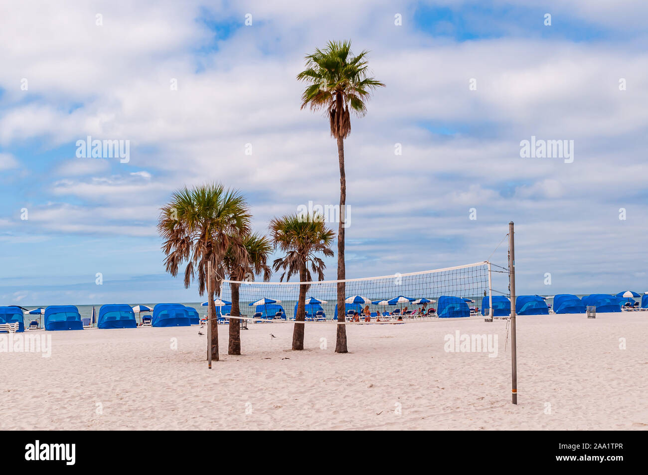 A volleyball net next to palm trees with tents on the beach in the
