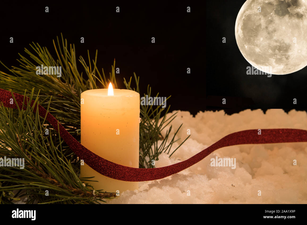 lit white candle and  pine needles in moonshine in snow. Black Christmas Background with warm holiday theme. Stock Photo