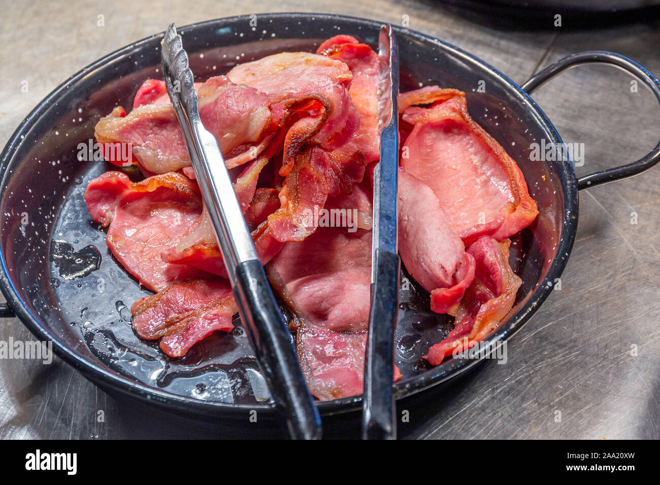 Pile of cooked back bacon in a serving skillet with tongs as part of a  hotel breakfast buffet Stock Photo - Alamy