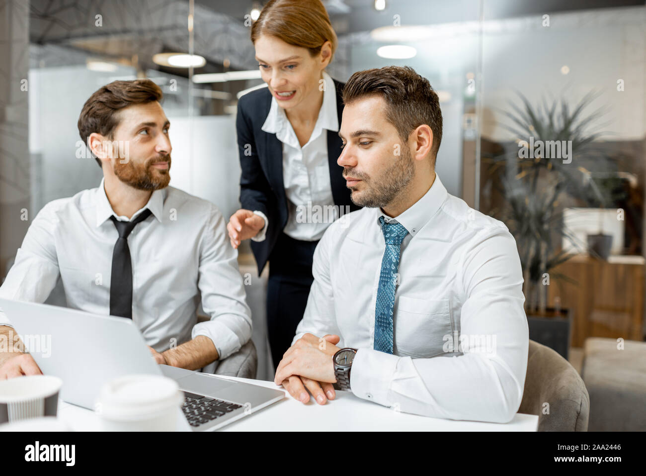 Team leader helping two male exhausted employees to do some work on a laptop in the office Stock Photo