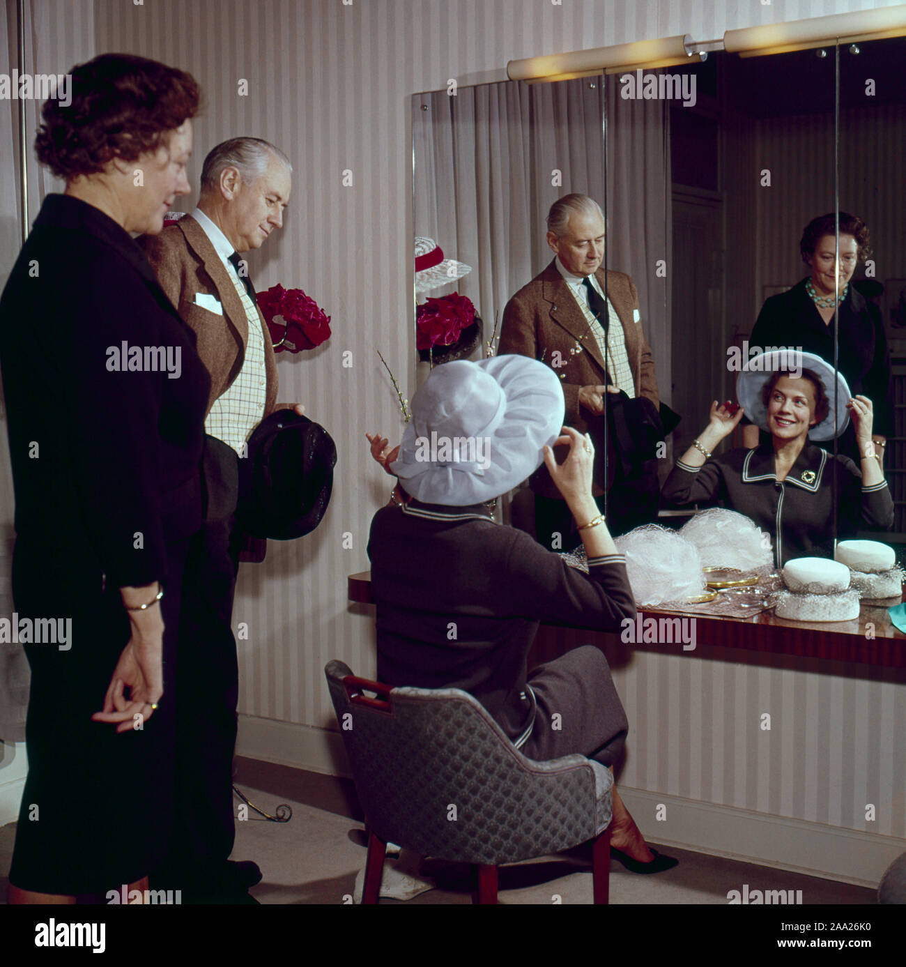 Trying out hats in the 1950s. A couple is sitting in front of a mirror trying hats on. He is humourist Erik Zetterström and she is Sickan Carlsson, actress. Sweden 1950s Stock Photo
