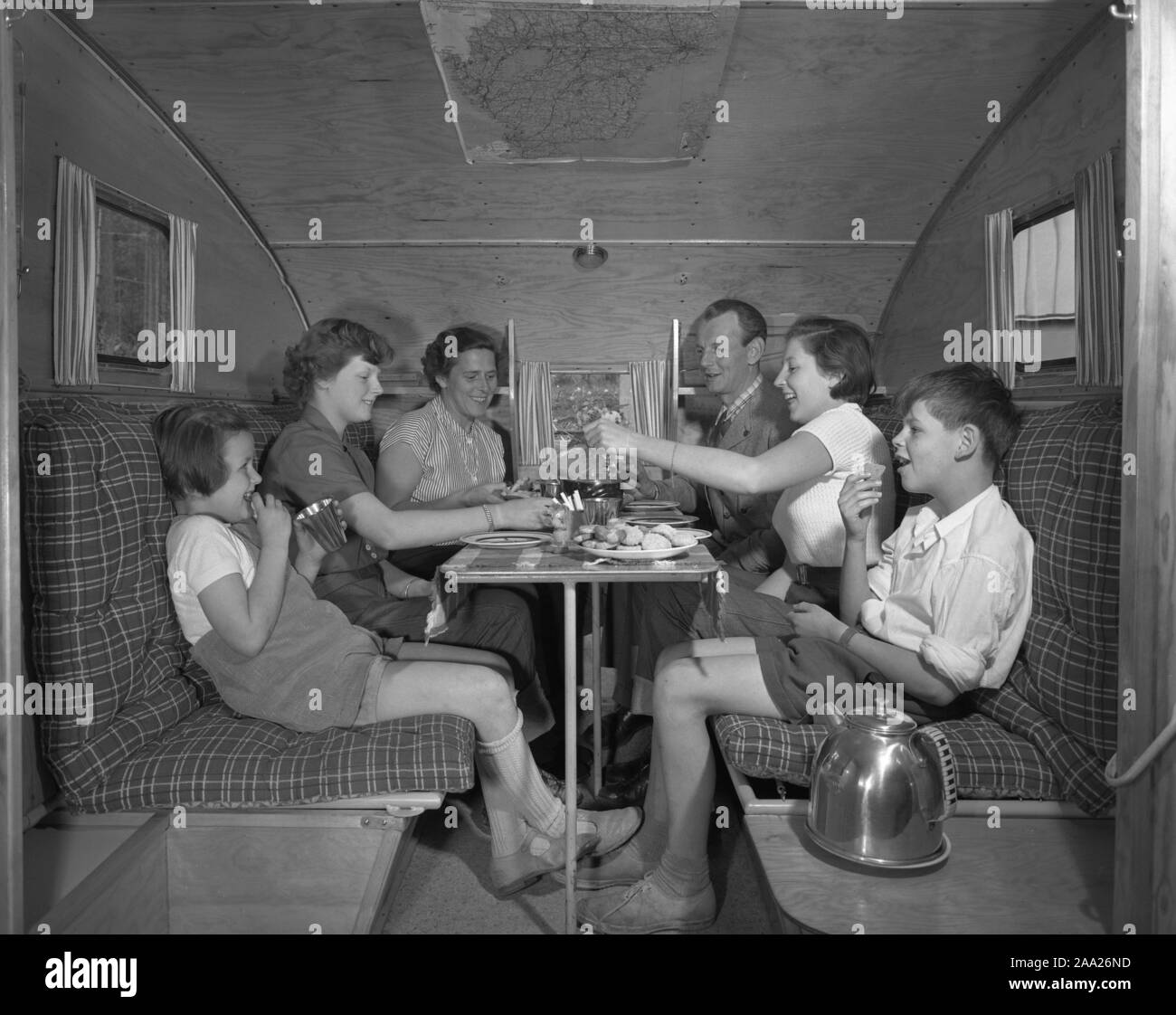 1950s camping. A family is enjoying their holiday and the practial camping life in their caravan. Demonstrating how well everything works for them even on holiday. The family of six people fits easily around the table. Sweden 1952 Ref 2021 Stock Photo