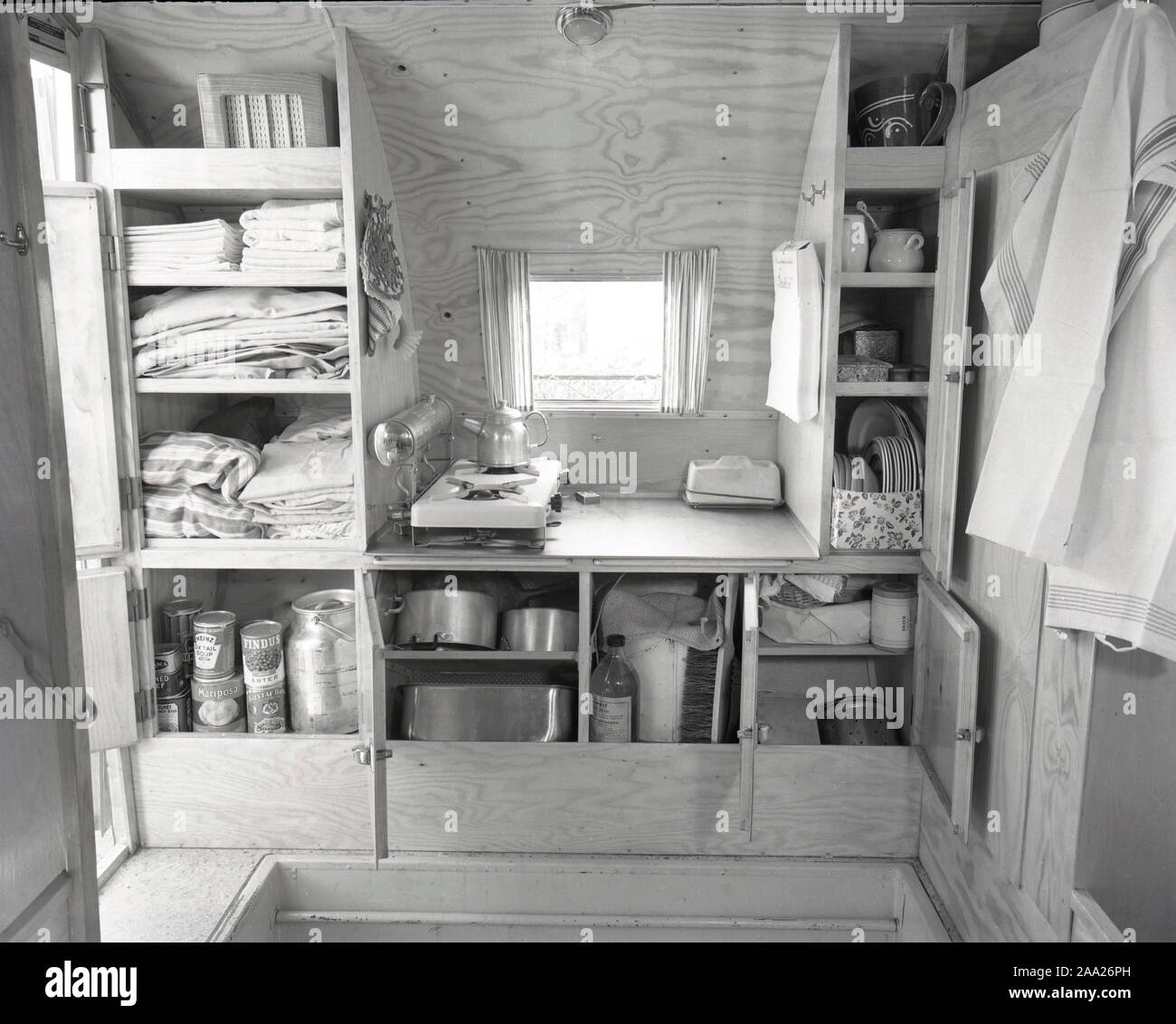 1950s camping. A family is enjoying their holiday and the practial camping life in their caravan. Demonstrating how well everything works for them even on holiday. The picture shows the practical storage for pots and pans, cups and plates. Sweden 1952 Ref 2021 Stock Photo