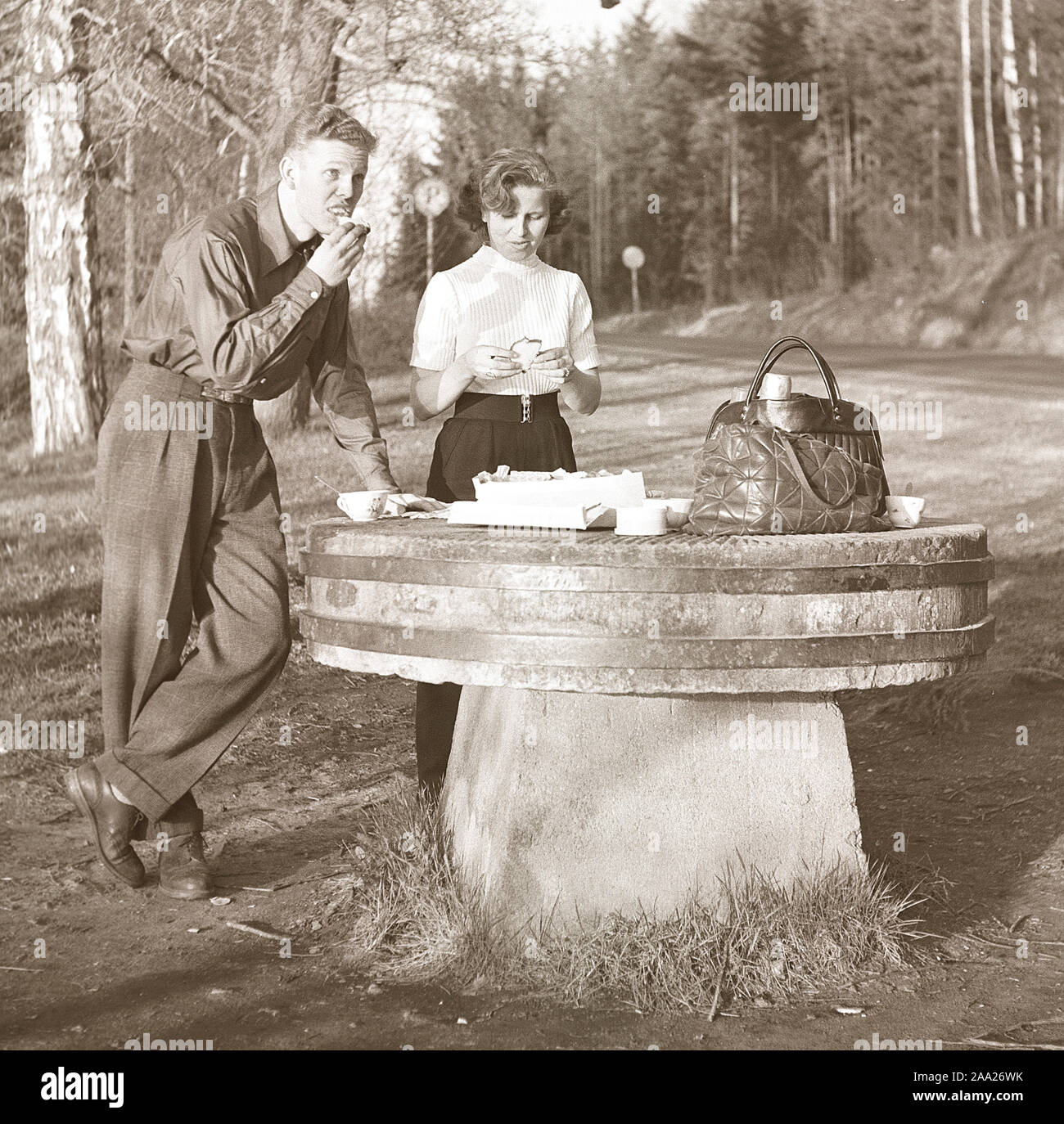 Lifestyle in the 1950s. A young couple has stopped to have a coffee Fika time and a sandwich by the roadside. An old millstone makes a good table for the picnic. Sweden 1952 Kristoffersson Ref BF76-4 Stock Photo