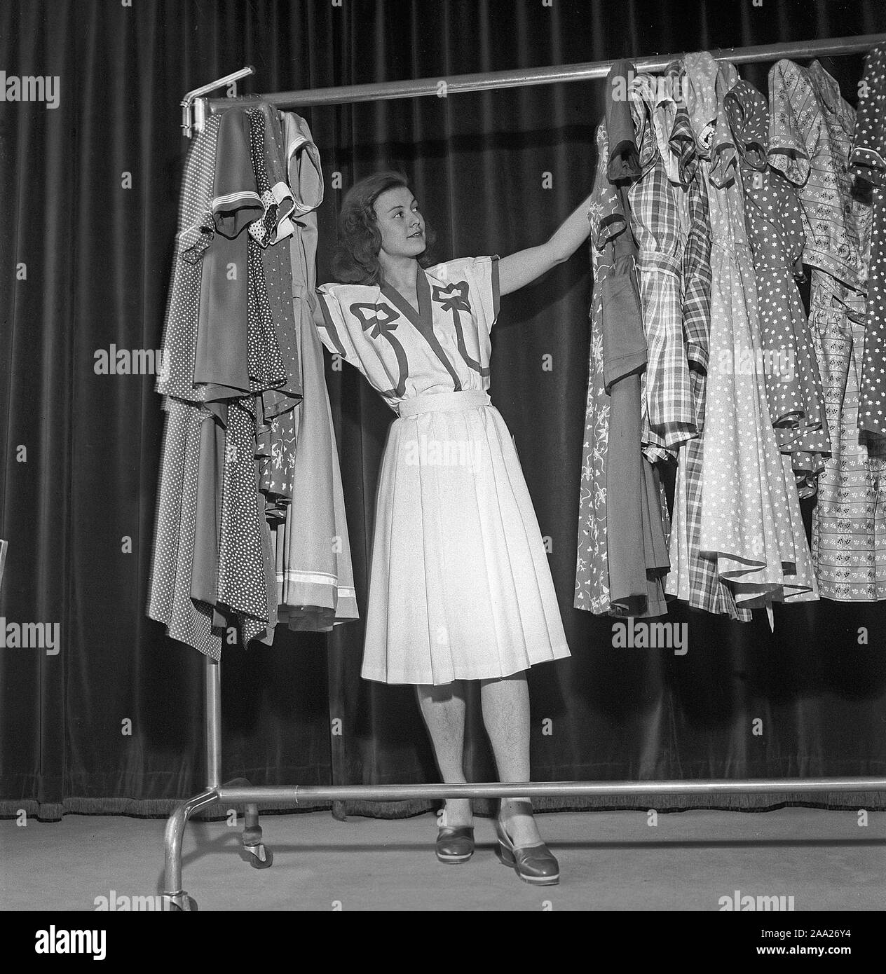 Women's fashion in the 1940s. A young woman in a typical 1940s outfit is standing and looking at different summer dresses. Sweden 1945 Kristoffersson Ref R129-1 Stock Photo