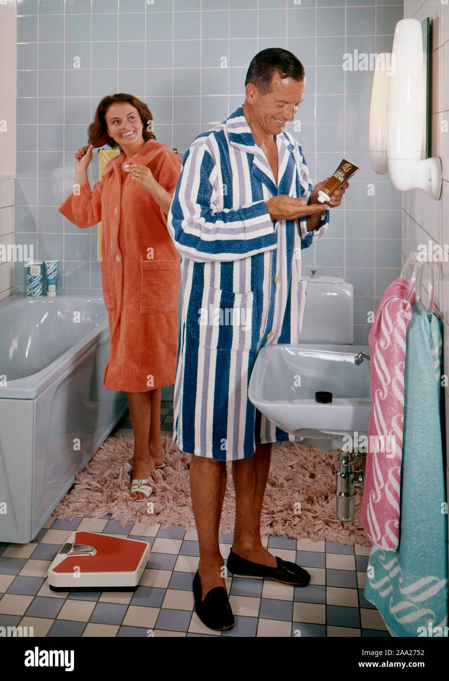 Bathroom of the 1960s. A couple in their typical 1960s bathroom. She in a orange bathrobe brushing her hair. Stock Photo