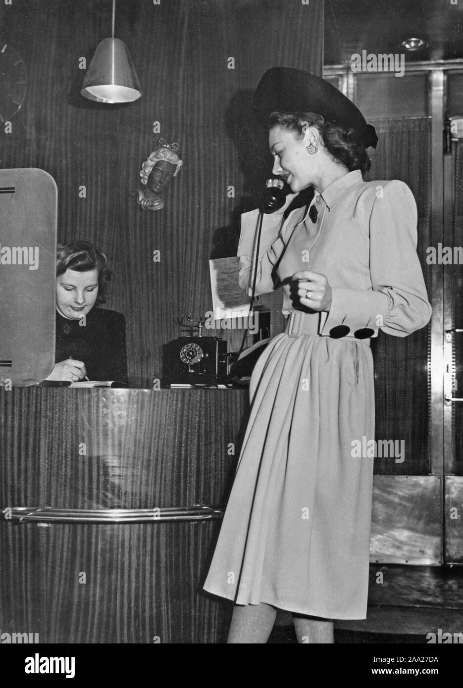 Women's fashion in the 1940s. A young woman in a typical 1940s outfit is talking on the phone. The summer dress is made by Williams fashion in Stockholm. Sweden 1947 Stock Photo
