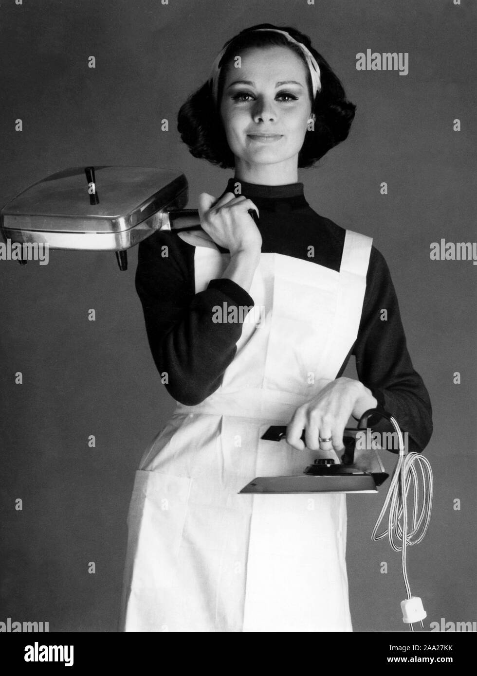 Back in the 1960s. A young woman is holding a flat iron and an electric whaffle iron made by Elektro Helios. Sweden 1963 Stock Photo
