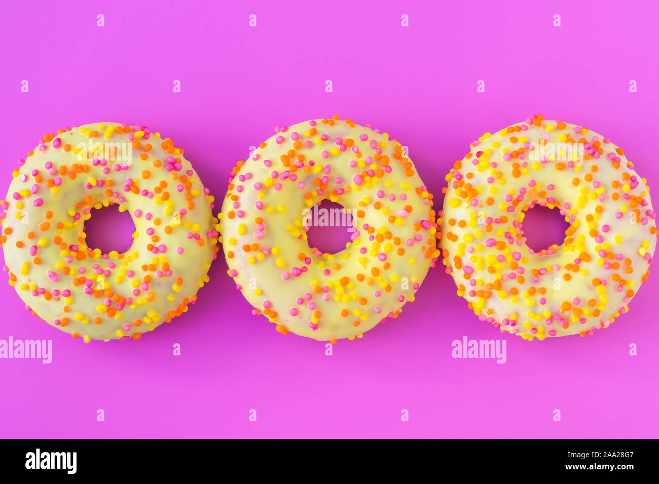 Three yellow round donuts with a hole on a pink background. Top view. Funny mood concept. Laconic food design. Stock Photo