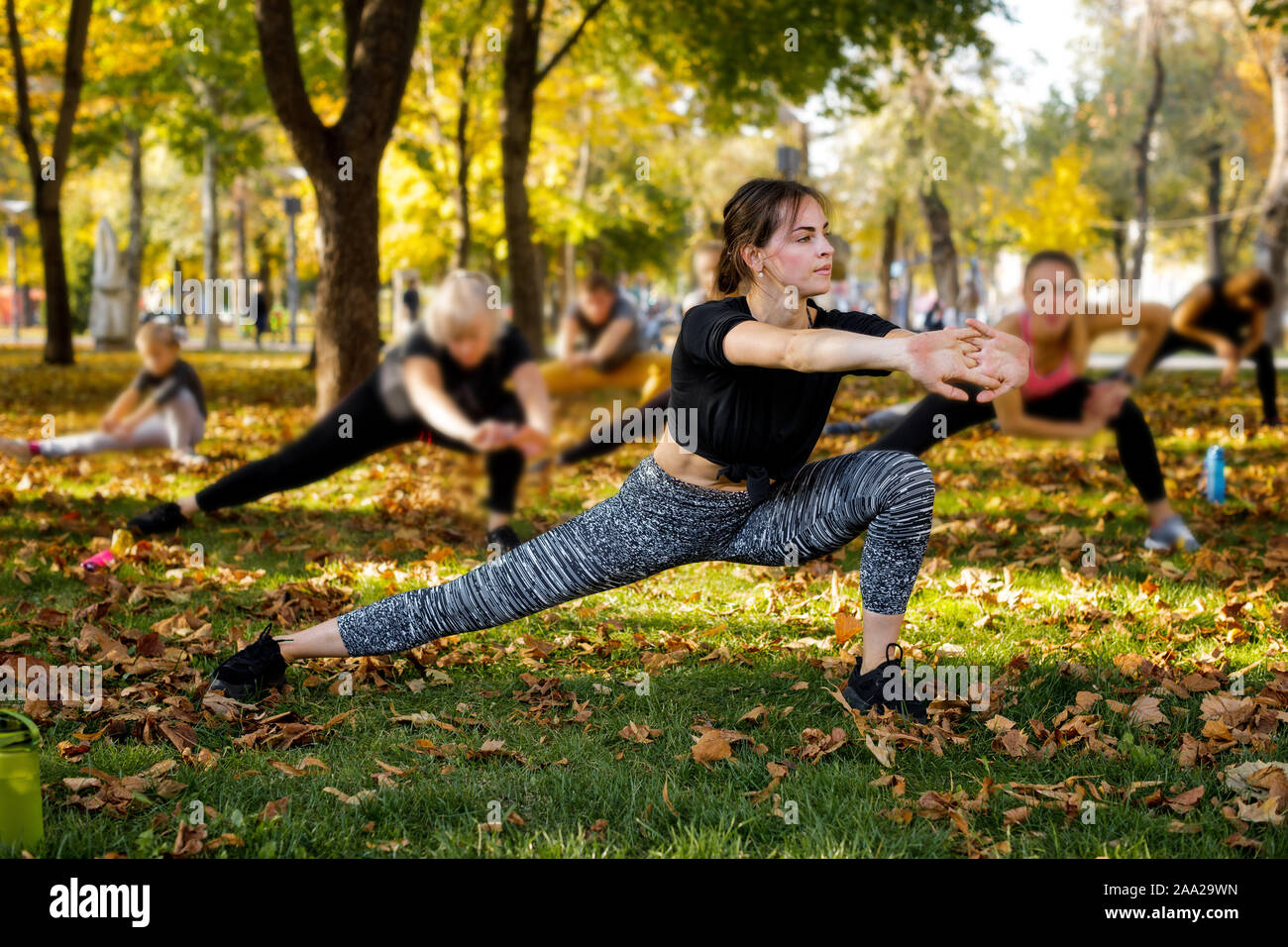 large group of people with trainer stretching on green grass in park Stock Photo