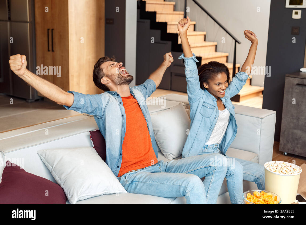Young adult woman and man raised hands up, sitting at home Stock Photo