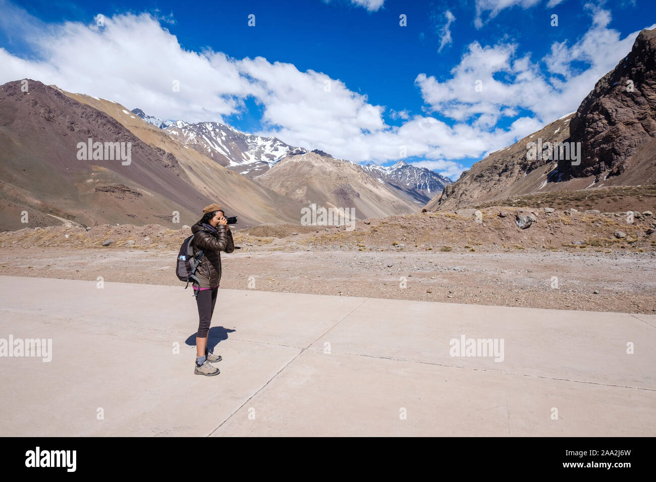 Female visitor photographing the Andean landscape on the high mountain road leading to the Aconcagua Park, Mendoza Province, Argentina Stock Photo