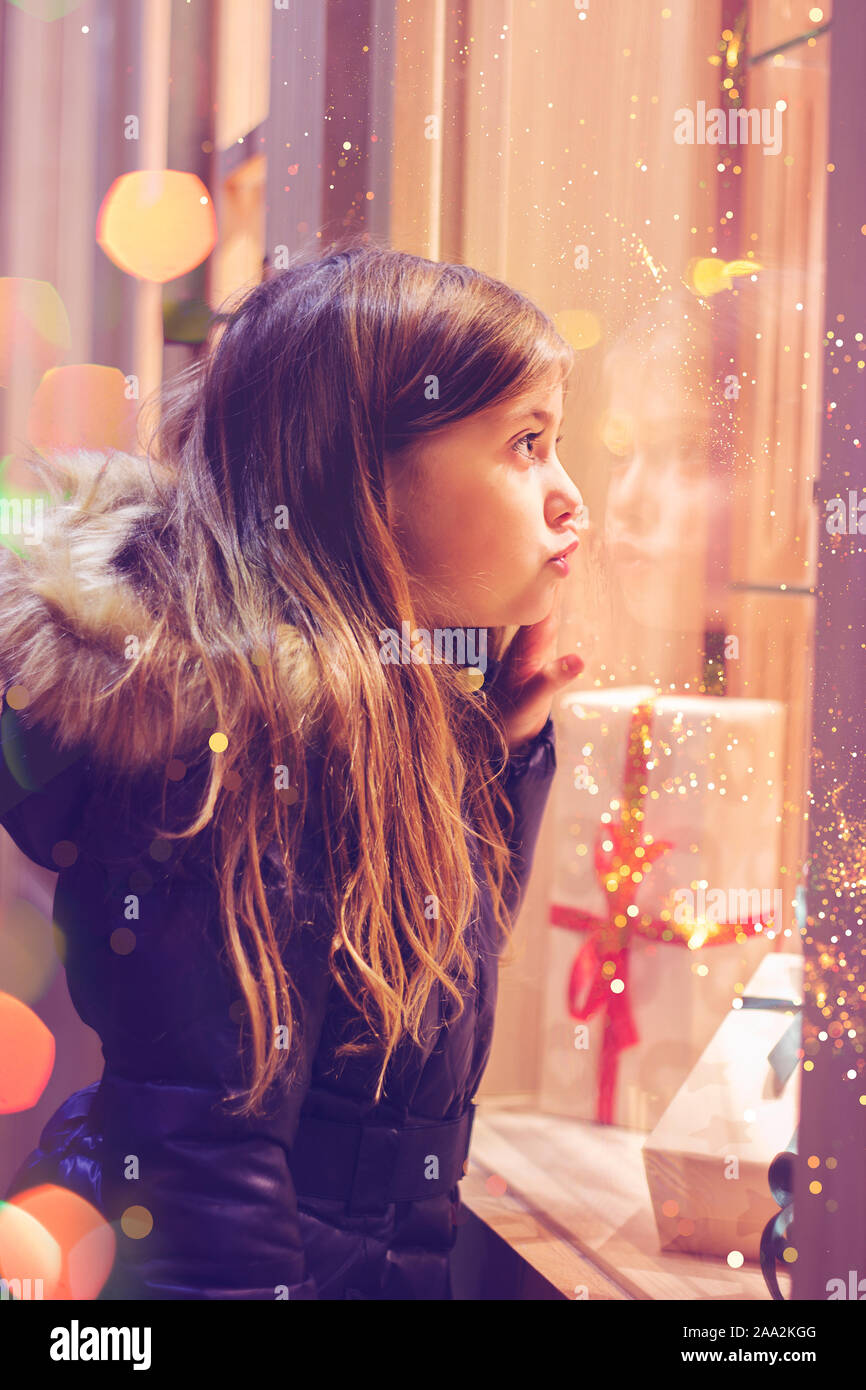 Beautiful little girl in front of confectionery shop, decorated with wrapped gift boxes and candies. Christmas concept, window shopping Stock Photo