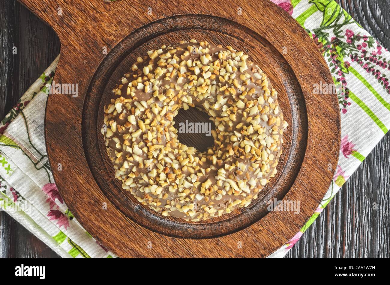 Delicious sweet snack served in a vintage style. Donut with a hole in chocolate topping with peanuts on dark wood. Stock Photo