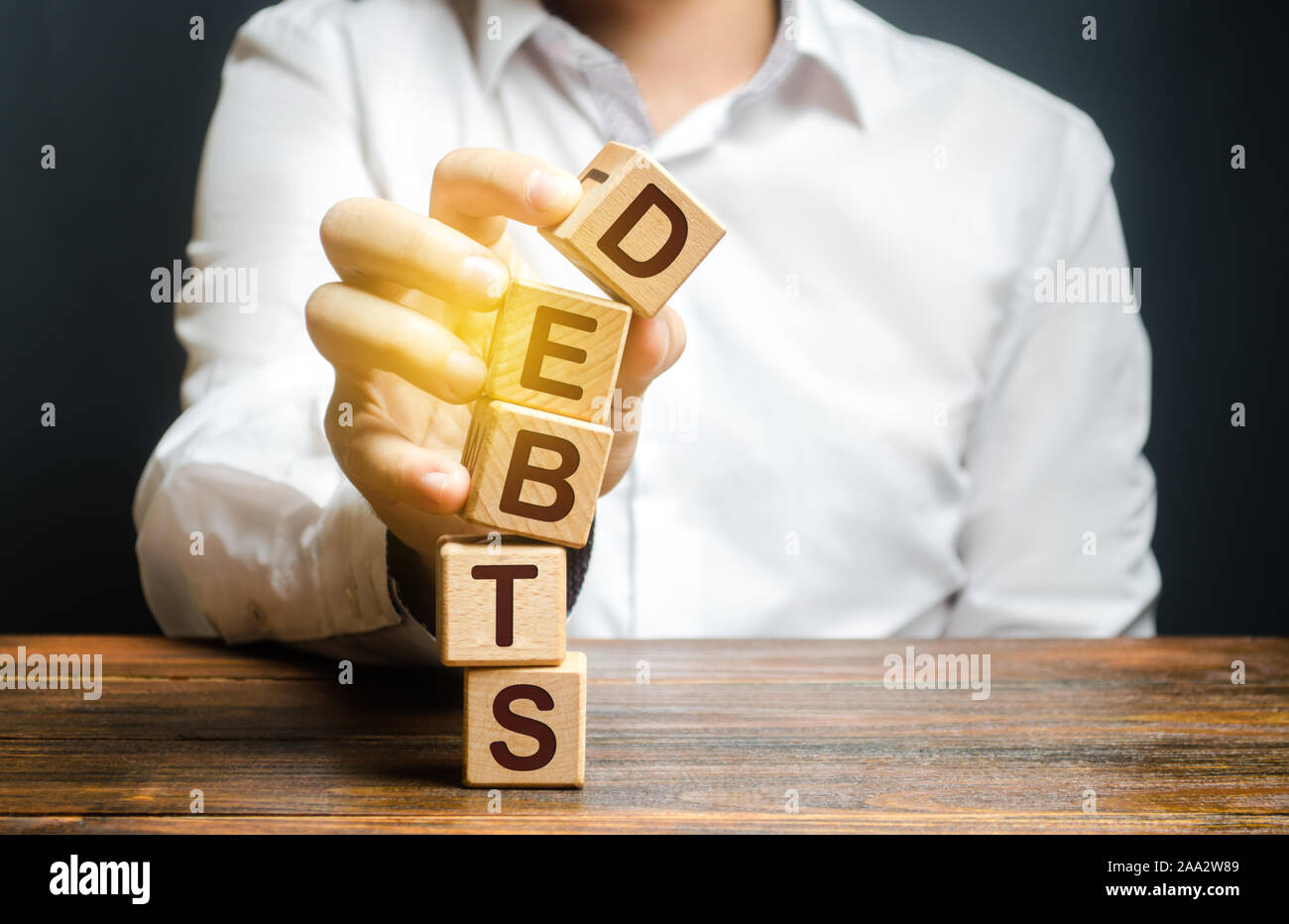 A man breaks a tower of blocks with the word Debts. Reduction or restructuring of debt. Bankruptcy. Refusal to pay. Heavily indebted citizens low fina Stock Photo