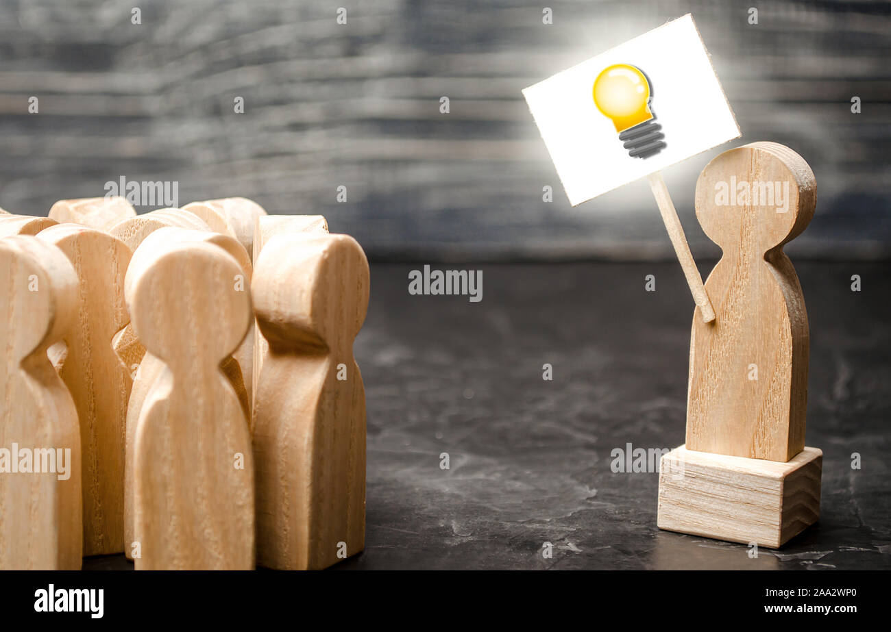 A person with an idea light bulb sign agitates a group of people. The concept of proposing new fresh ideas, finding a solution. Creativity, leadership Stock Photo