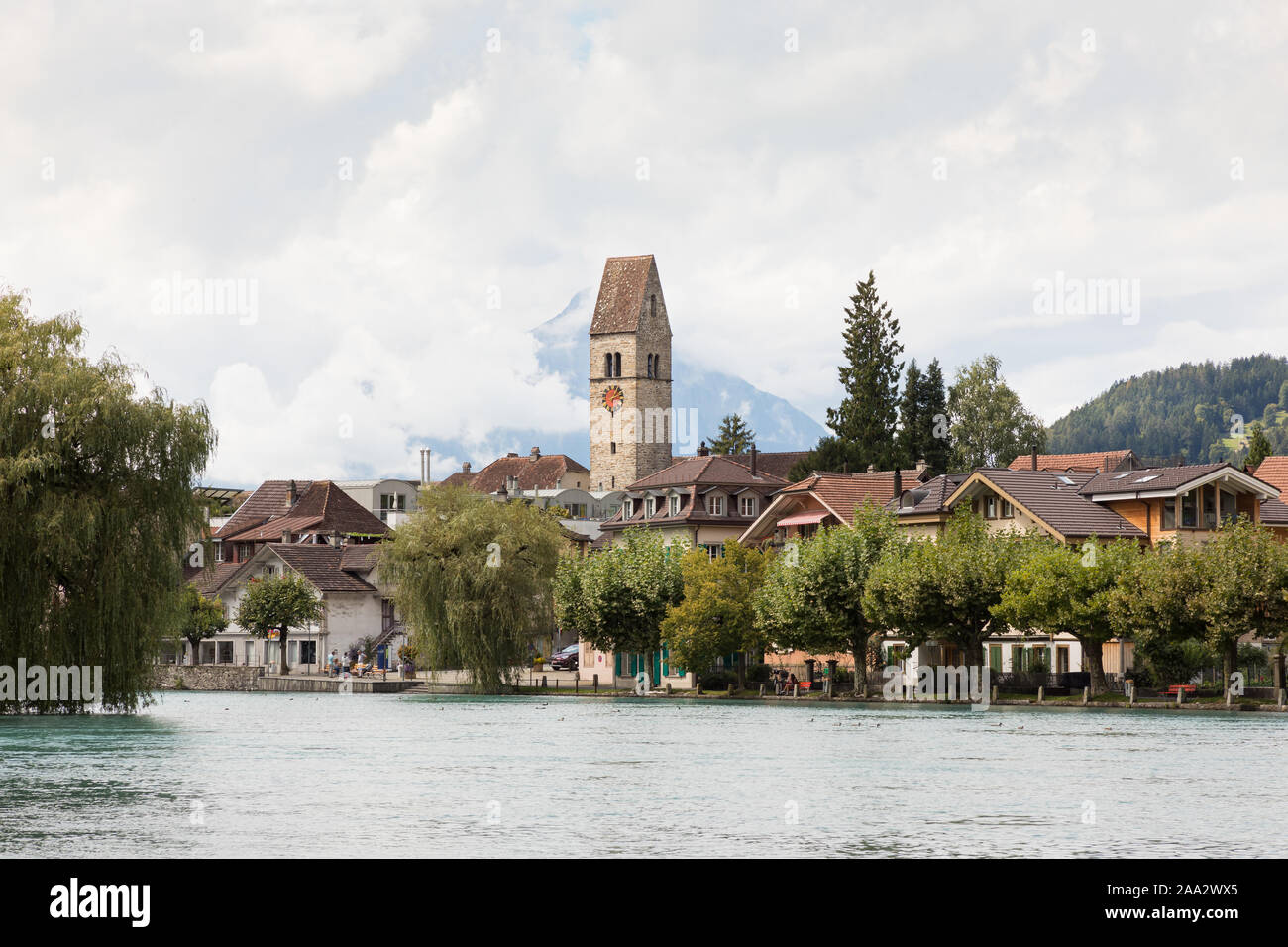 Unterseen, Interlaken, Switzerland: Trees line the bank of the river Aare, behind which the tower and clock of the old church rise above the rooftops. Stock Photo