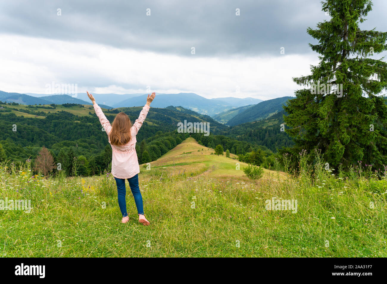 Happy woman standing on green hill and looking at mountains Stock Photo
