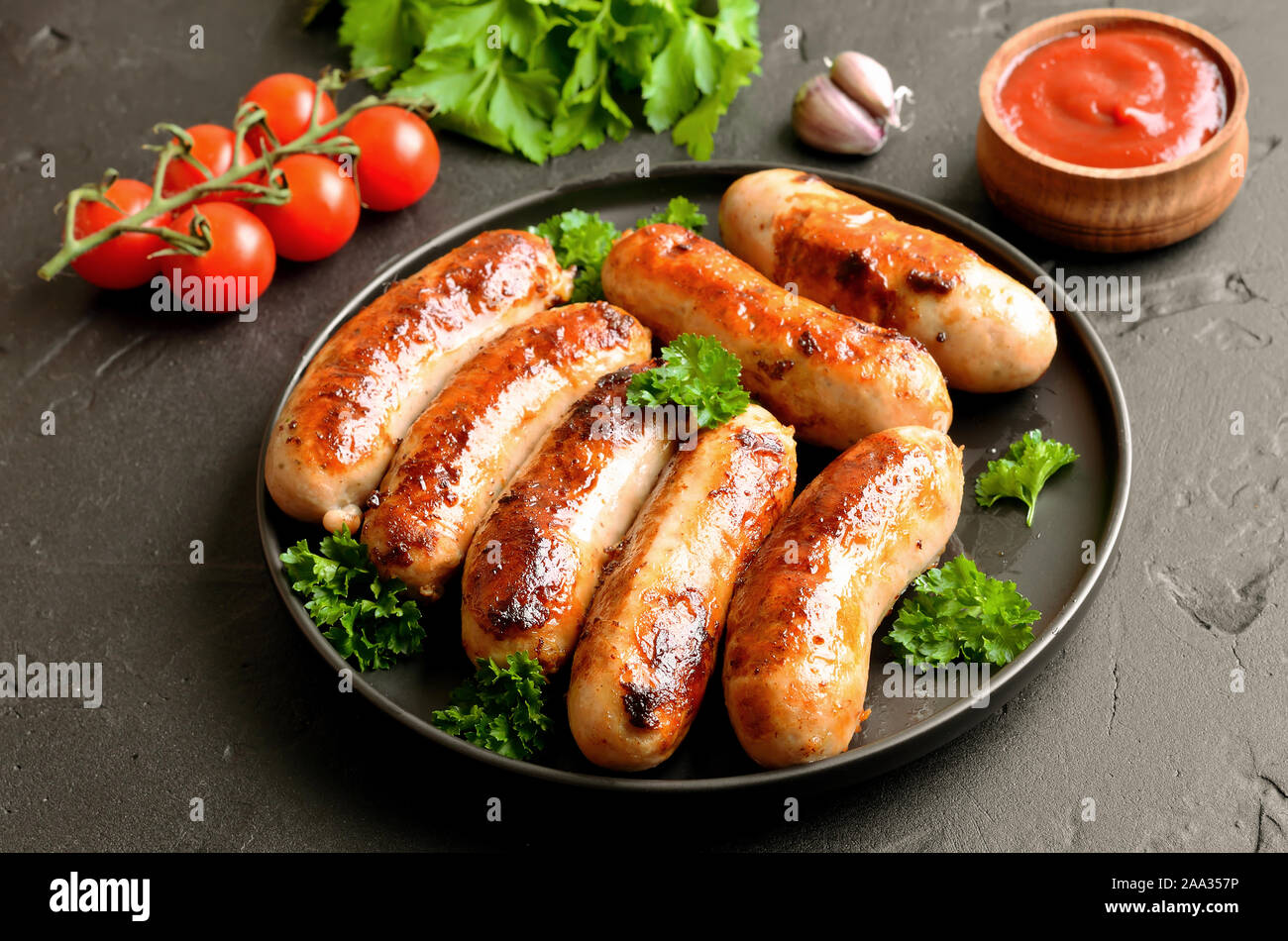 Barbecue sausage with fresh parsley on plate, fresh tomatoes and garlic on table Stock Photo