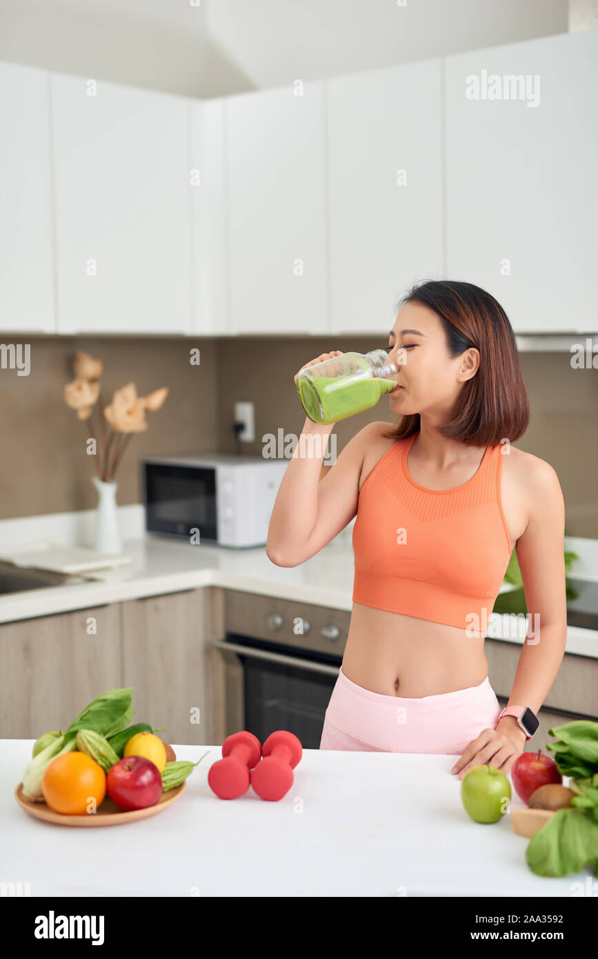 Pretty Asian woman drinking green detox juice while wearing sportive clothing Stock Photo