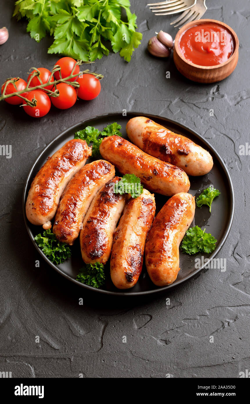 Fried sausage with fresh parsley on plate, fresh tomatoes and ketchup on table Stock Photo