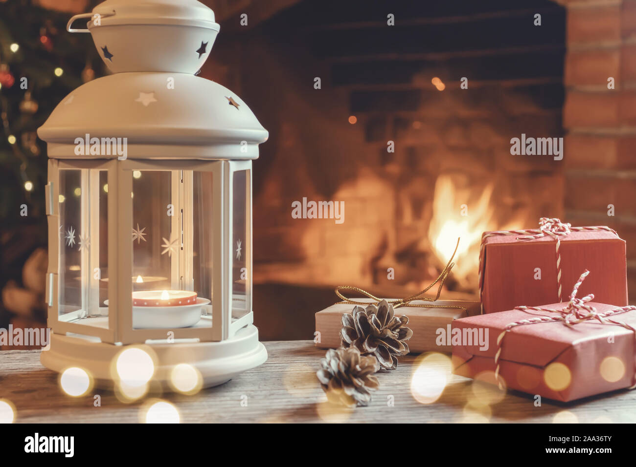 Lantern with a burning candle, gifts on a wooden table in a room with a Christmas tree and a fireplace on Christmas Eve. Stock Photo