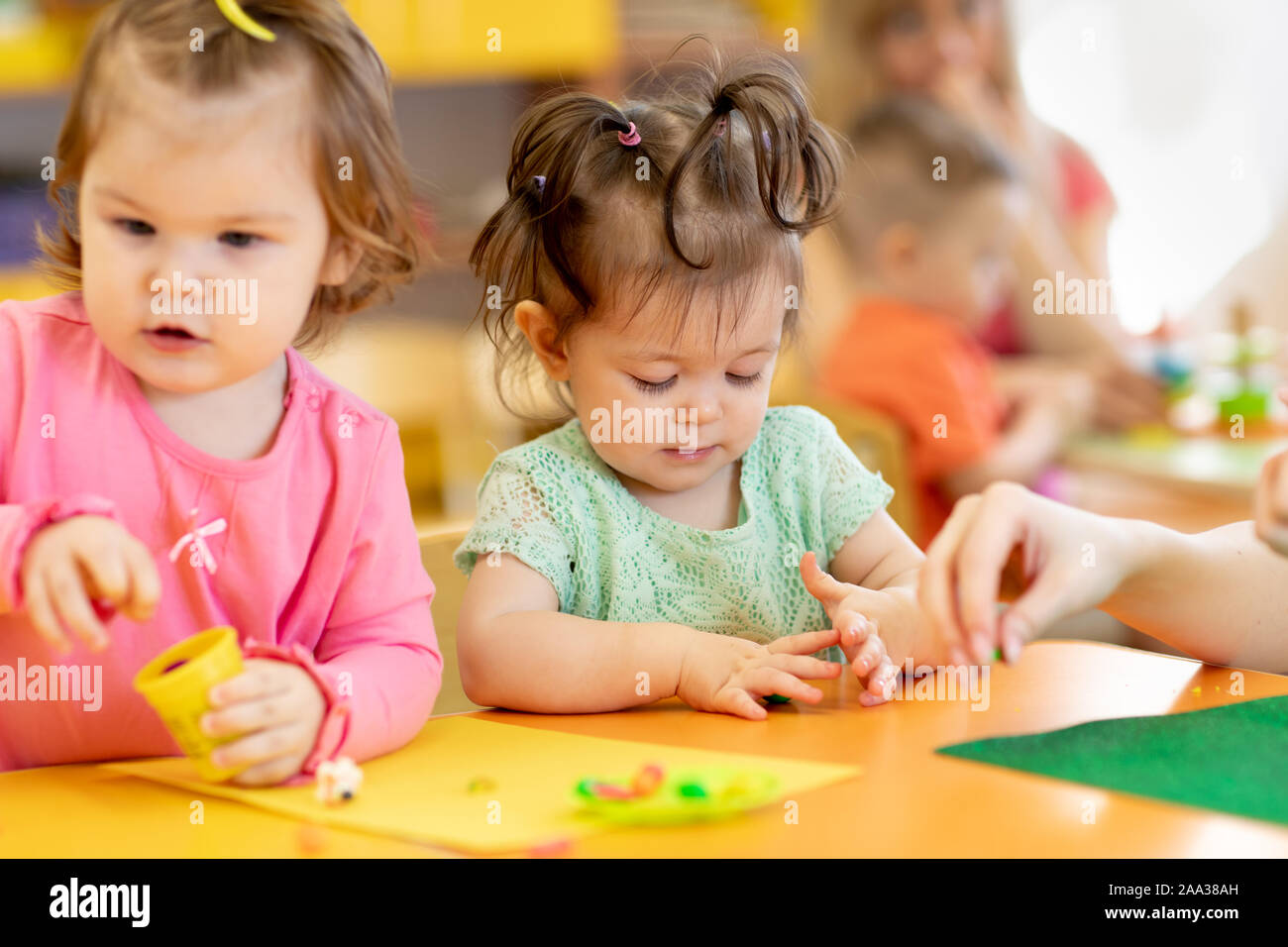 Little kids having fun together with colorful modeling clay at daycare. Children playing with plasticine or dough. Stock Photo