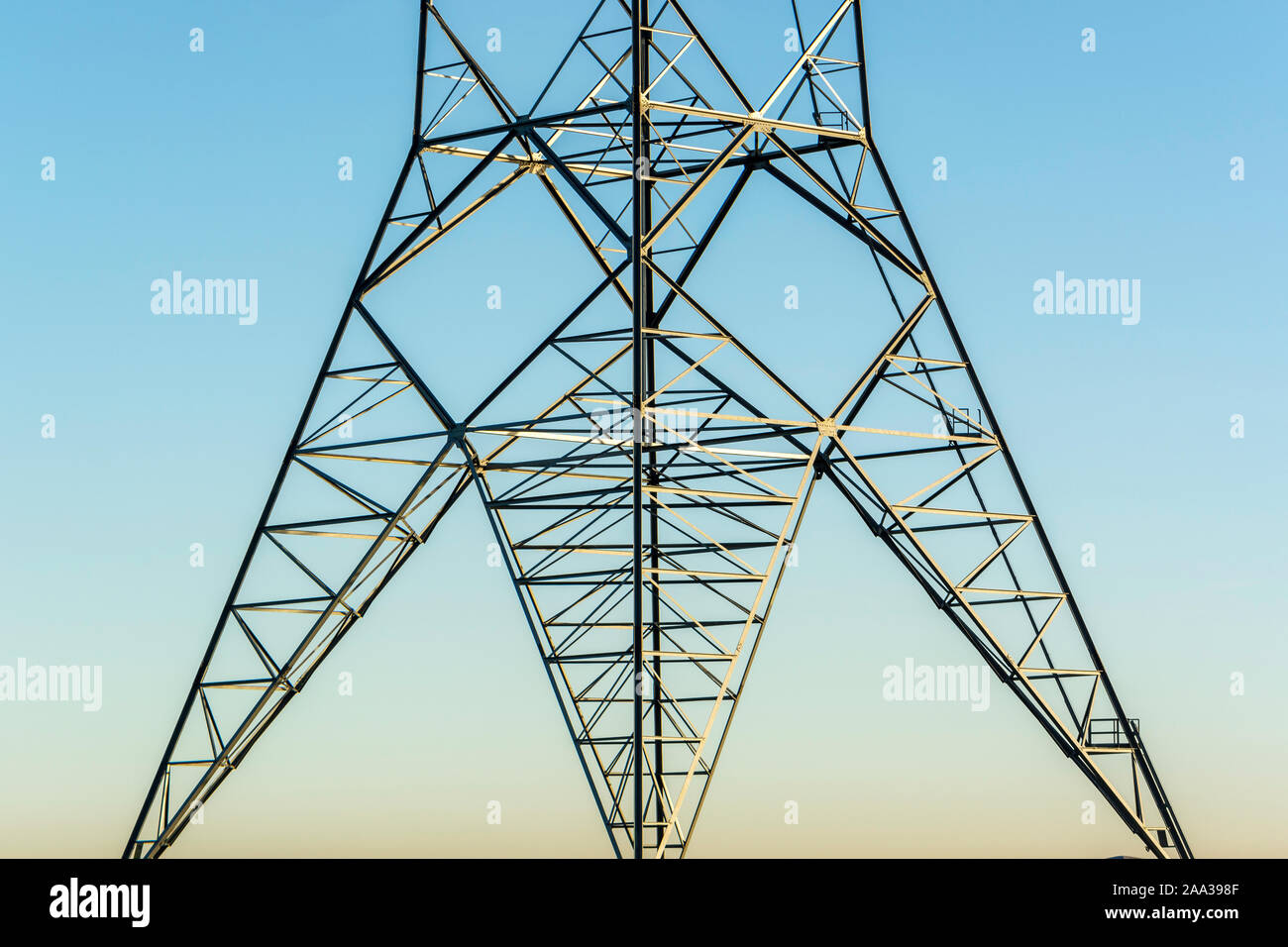 Electricity mast, electricity pylon,  abstract concept, transporting wind energy, electric lines on the background of blue and orange sky, sunny morni Stock Photo