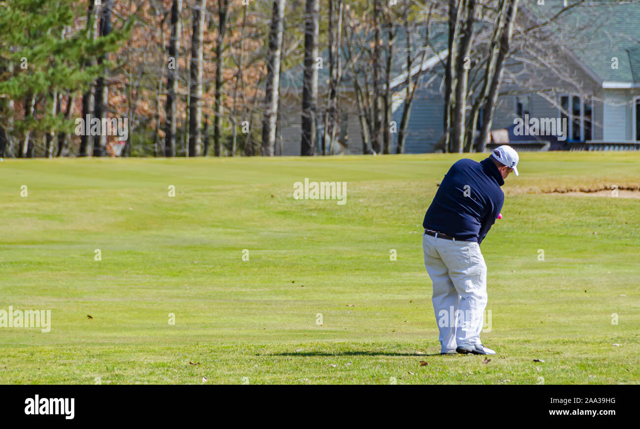 A golfer hitting a golf ball on the fairway towards the putting green. Stock Photo