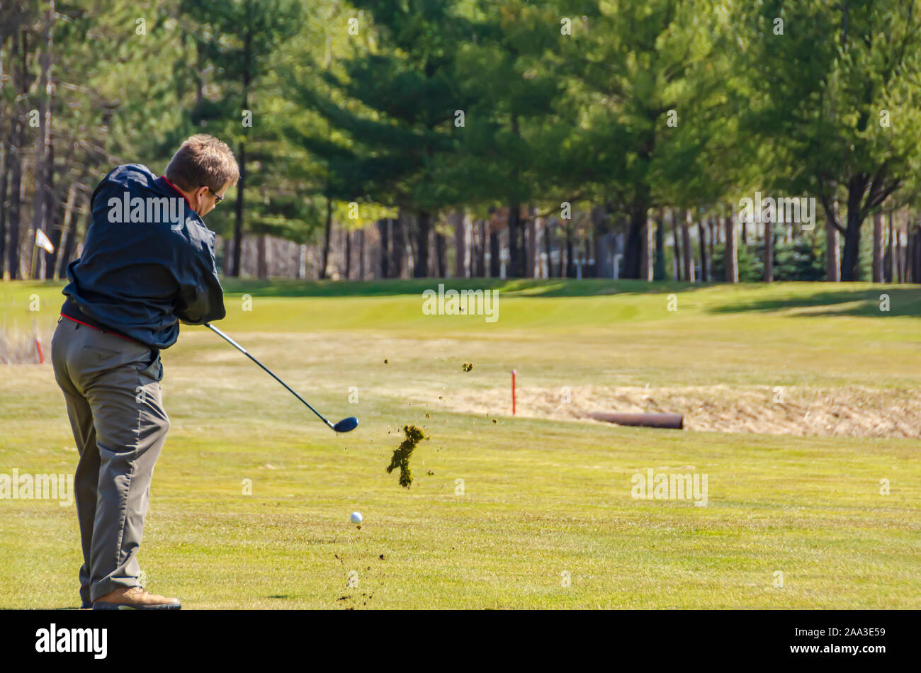 A golfer hitting a golf ball on the fairway with a hybrid golf club. Stock Photo