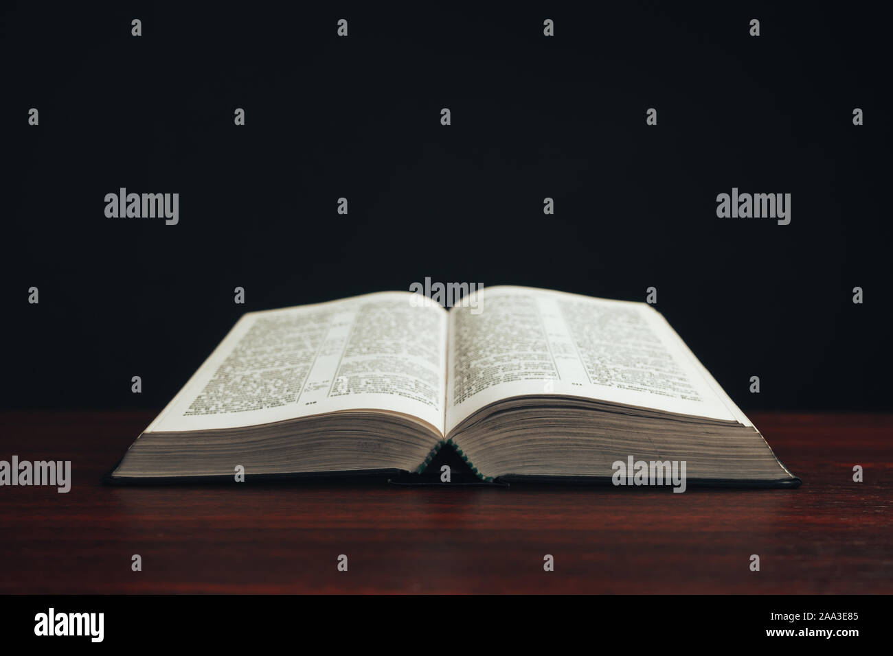 Open bible on a  red wooden table. Beautiful black background. Stock Photo