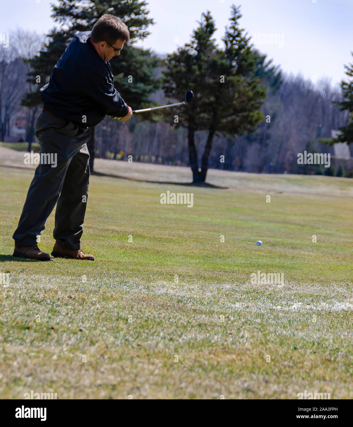 A golfer hitting a golf ball on the fairway with a hybrid golf club. Stock Photo
