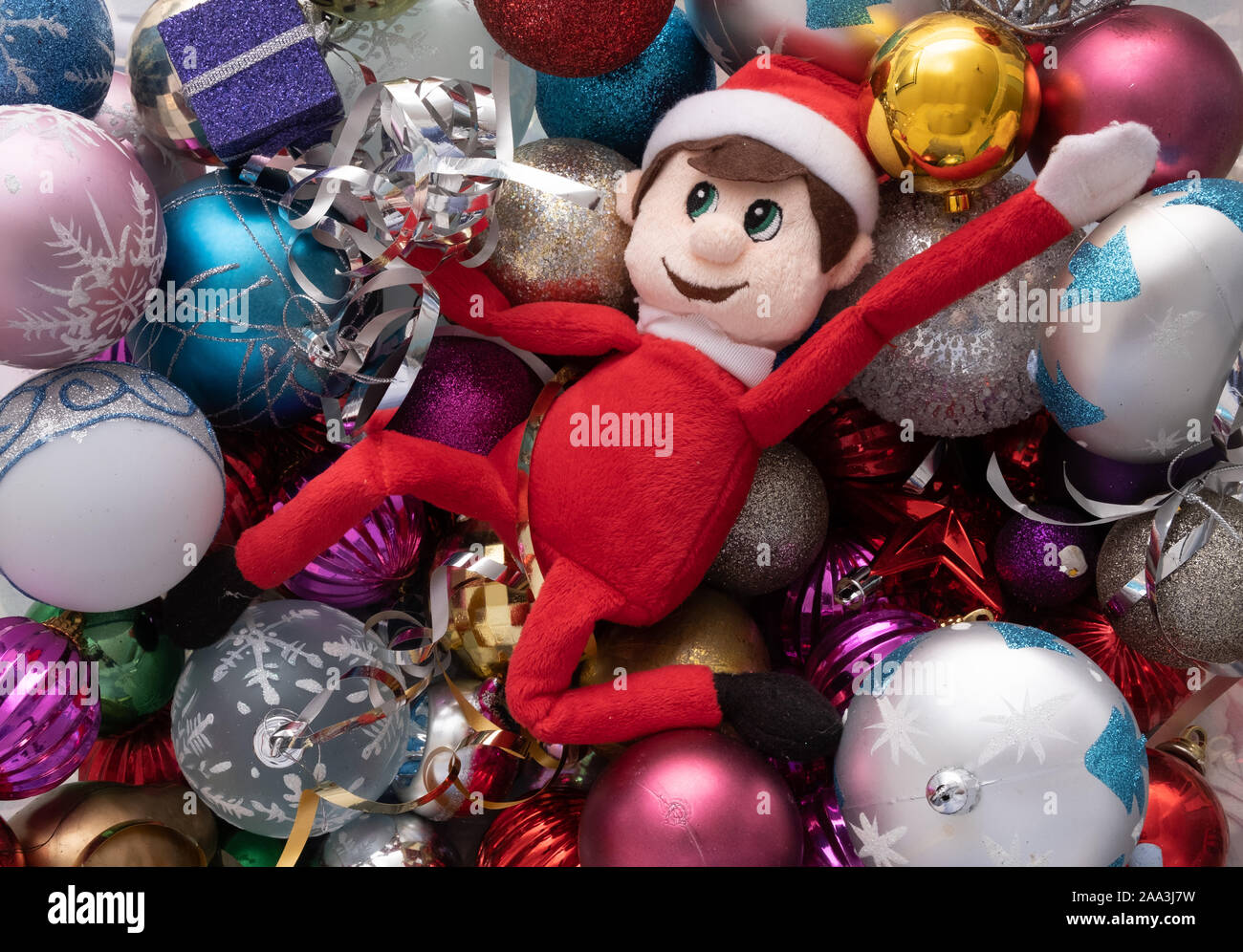 Elf on the shelf being naughty playing in a ball pond of christmas baubles. Cute tradition of sending Santa's elf to check up on children just before Stock Photo