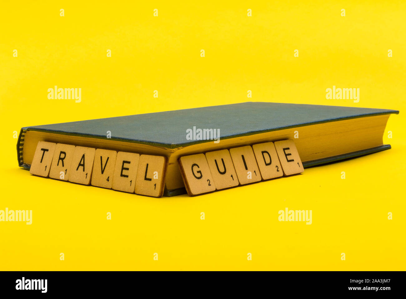 Travel concept showing a book with a sign reading travel guide on a yellow background Stock Photo