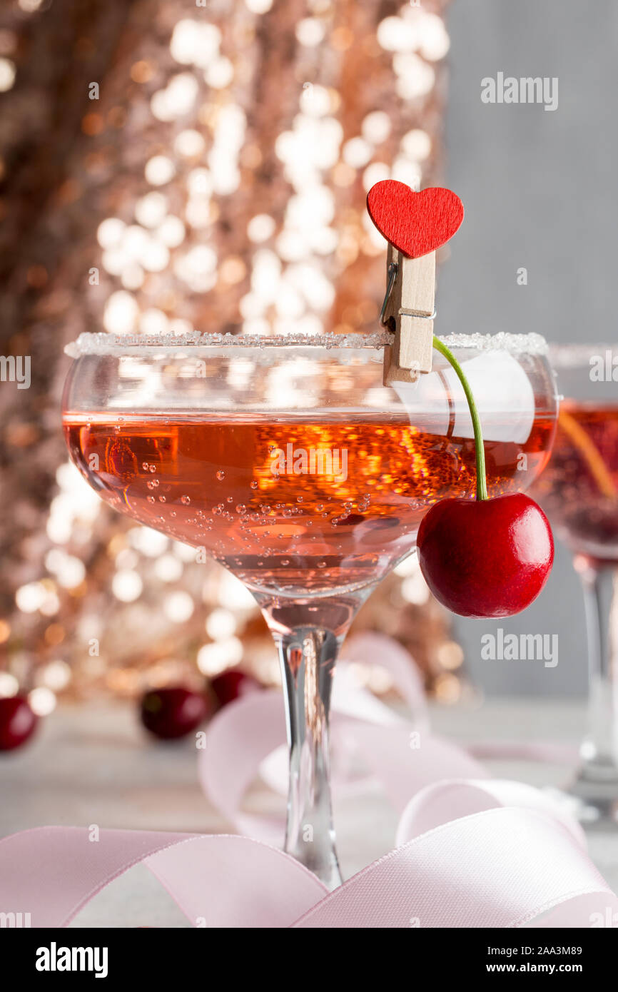 Two beautiful glasses with pink champagne and sweet cherry with heart shaped pin on it. Concept of shine party drinks Stock Photo