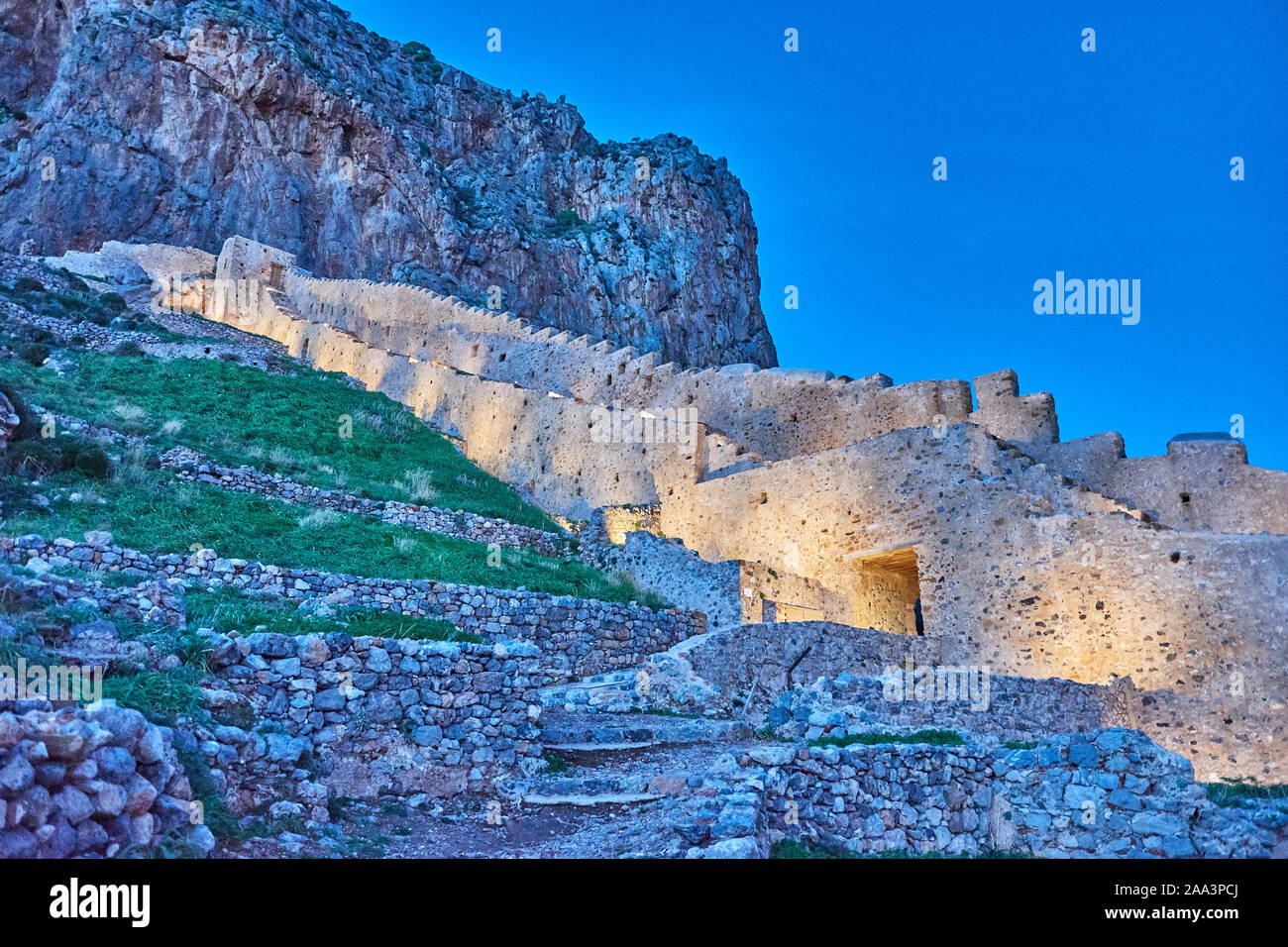 Illuminated Stone walls into the picturesque castle town of Monemvasia at night. Architectural buildings and beautiful narrow paved streets. Stock Photo