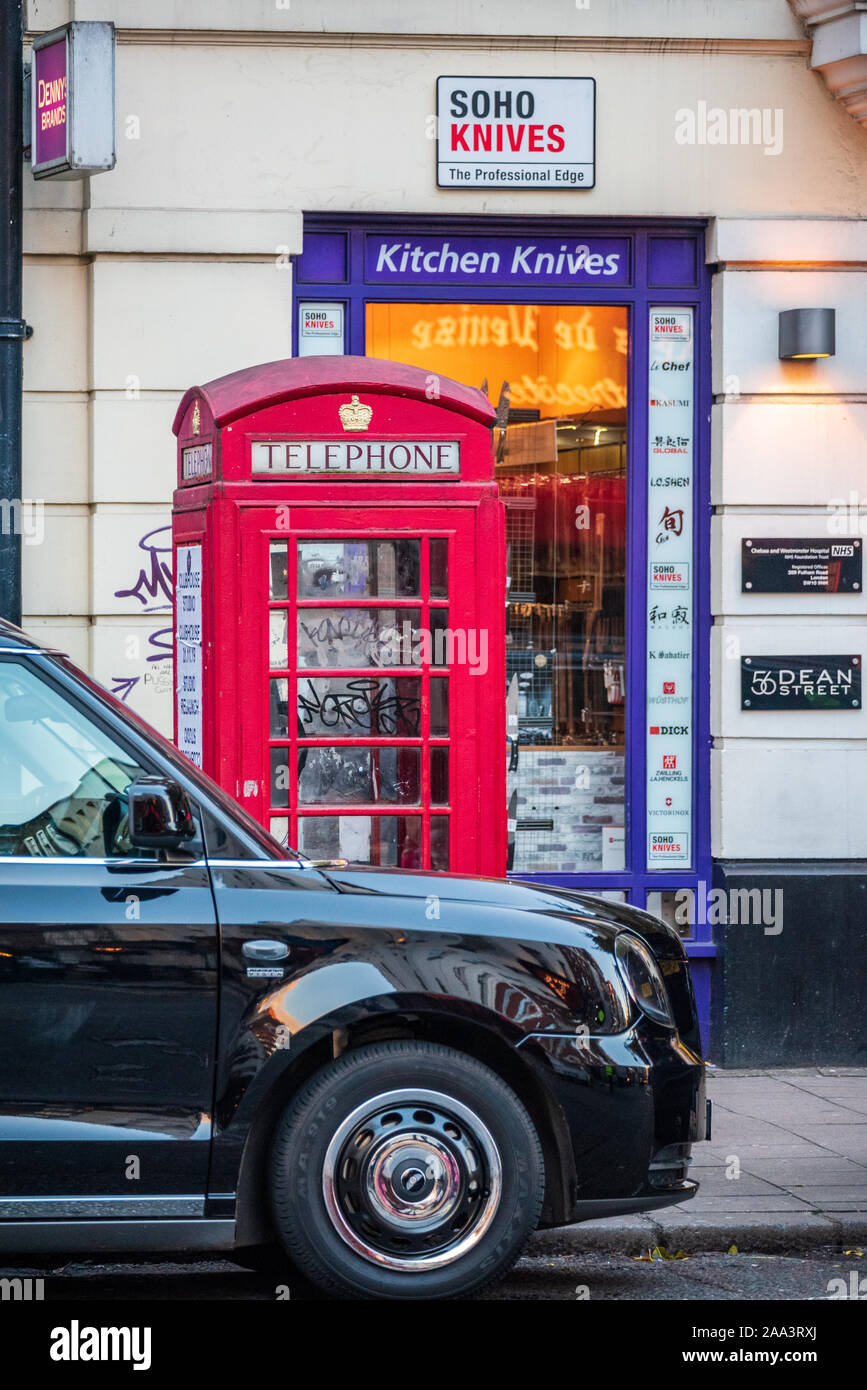 Soho London Dean Street. An electric taxi in front of a red telephone box in fromt of the Soho Knives store in London's Soho entertainment district. Stock Photo