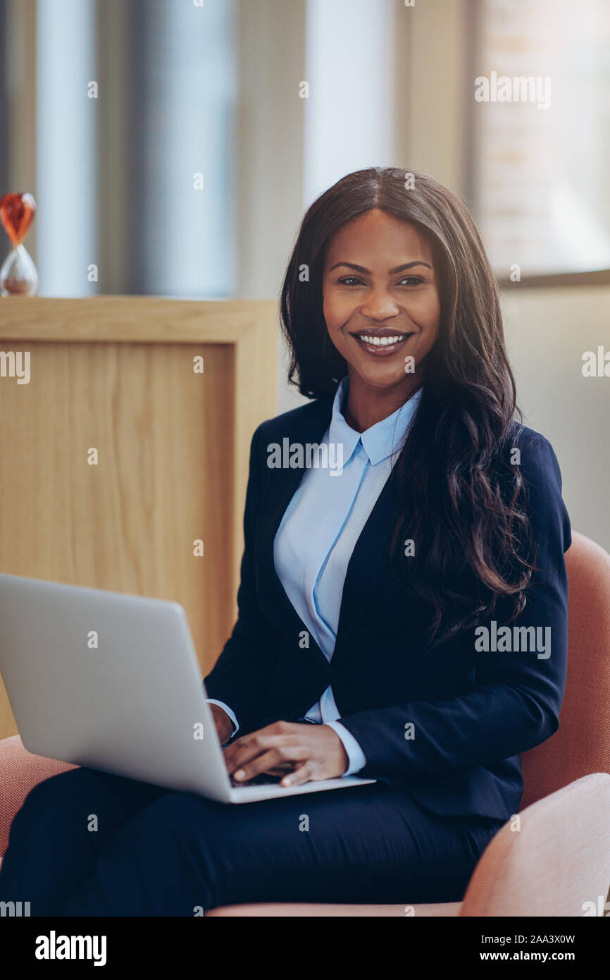 Smiling young African American businesswoman sitting in a chair in the ...