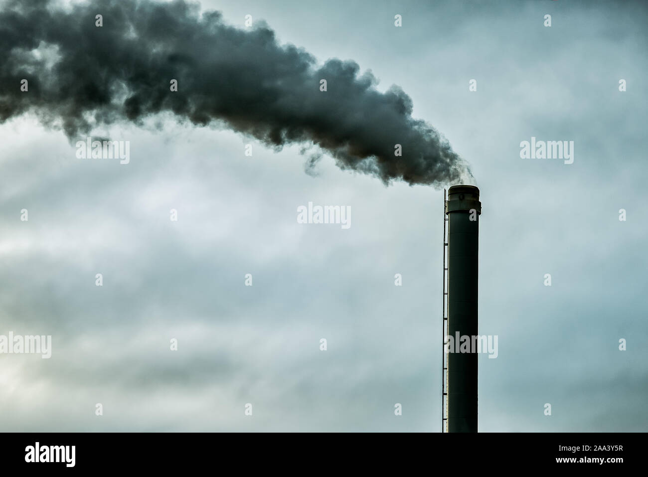 Black smoke on a grey sky with space copy , comming from a tall chimney. Denmark, November 10, 2019 Stock Photo