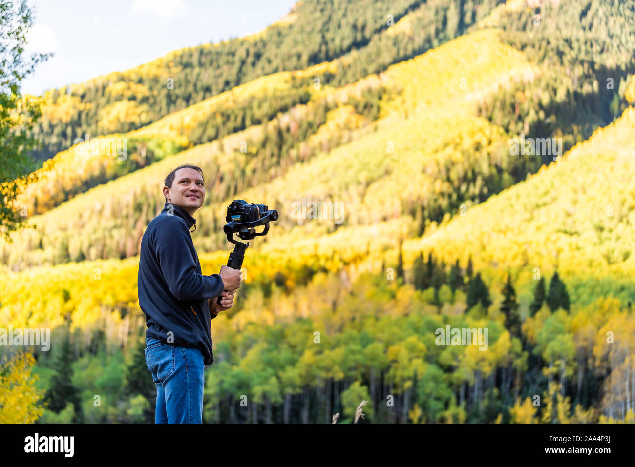 Castle Creek road view with happy man holding camera gimbal filming colorful yellow leaves foliage on aspen trees in Colorado rocky mountains autumn f Stock Photo