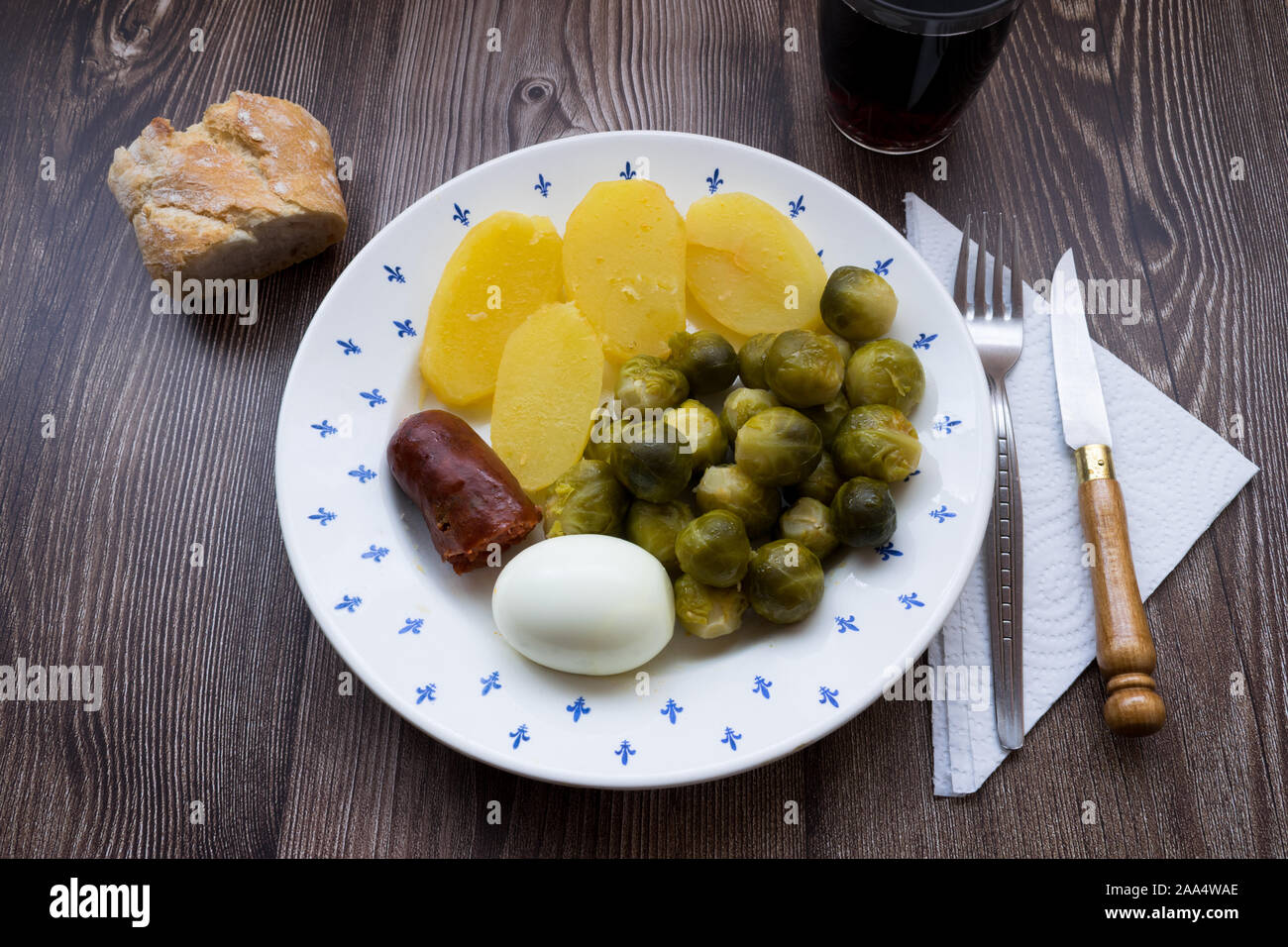 Plate with brussel sprouts, sausage, cooked potatoes and egg on a wooden table. Traditional Spanish food Stock Photo