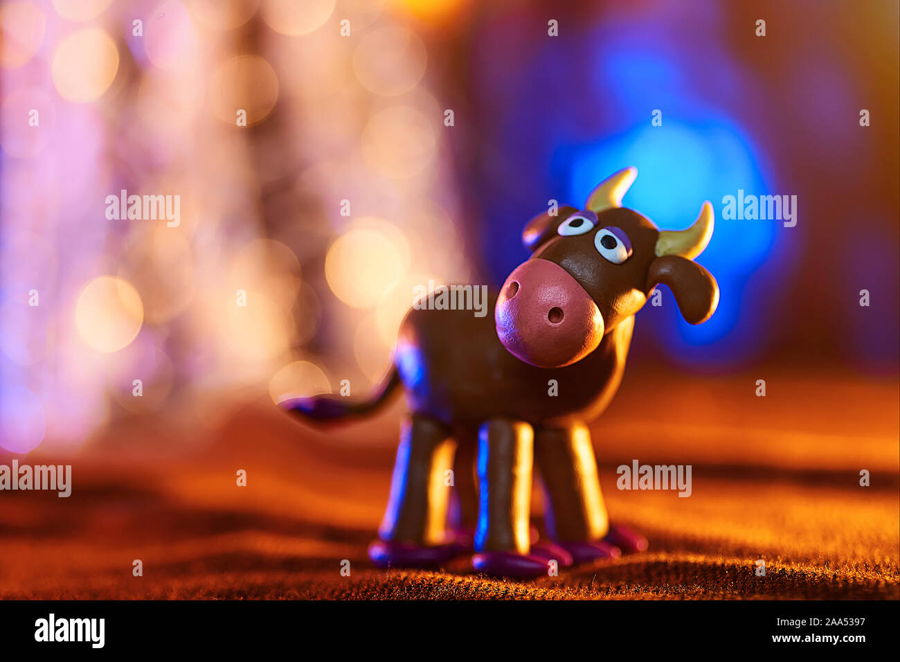 Christmas cow from plasticine on the background of lights Stock Photo