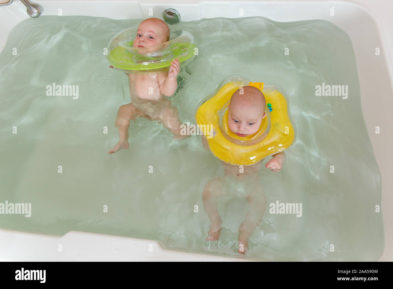 Newborn twins swimming in the bath or bathtub. Inflatable circle helps