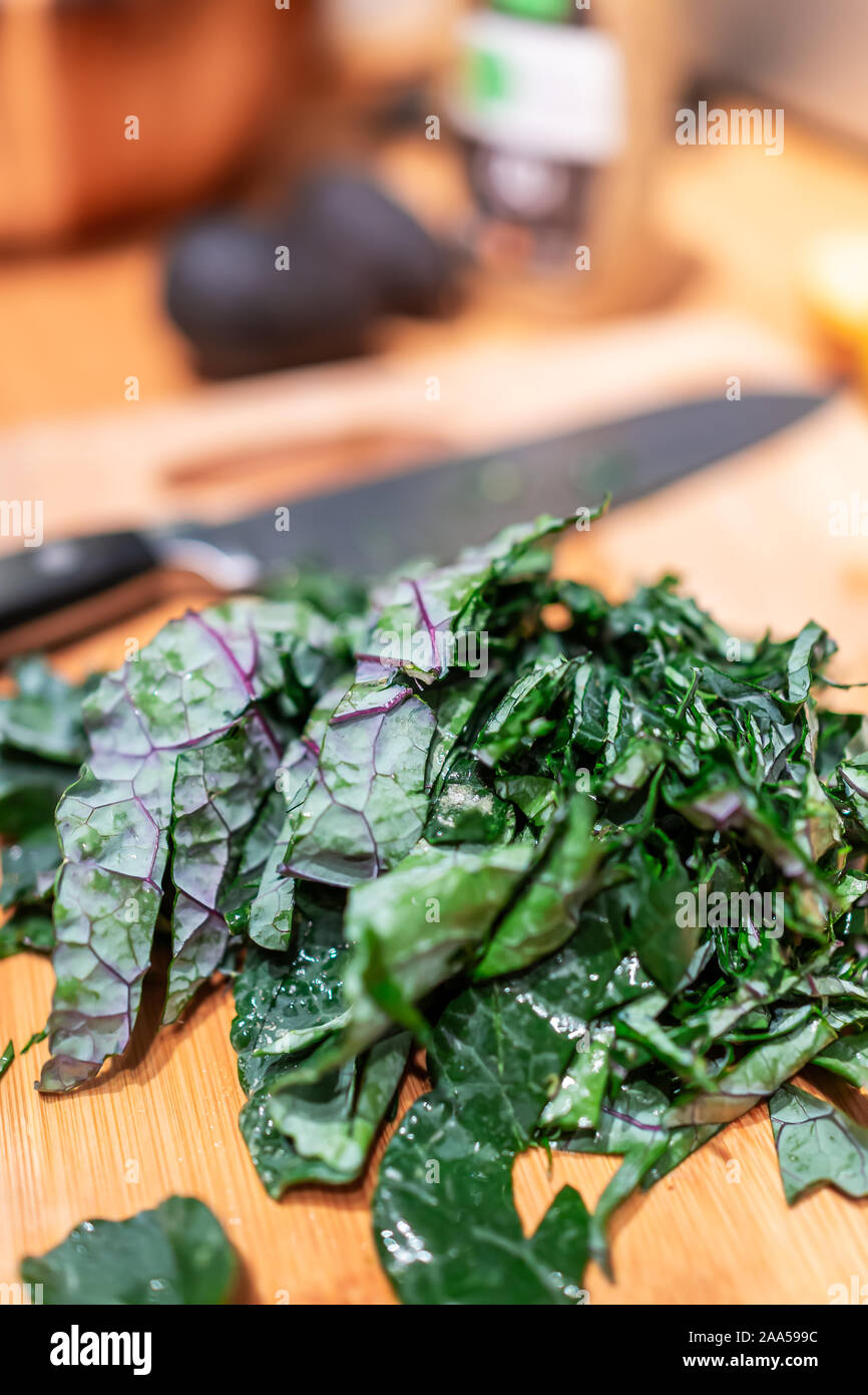 Chopping board with chopped green red kale leaves in kitchen vegetables for healthy meal cooking preparation and knife in background Stock Photo