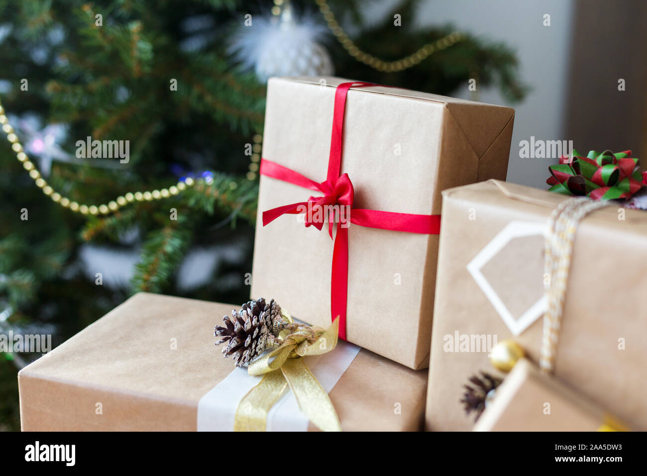 Gift boxes with christmas tree at background. Red, golden and white ribbons on craft present boxes. Festive Christmas tree on background Stock Photo