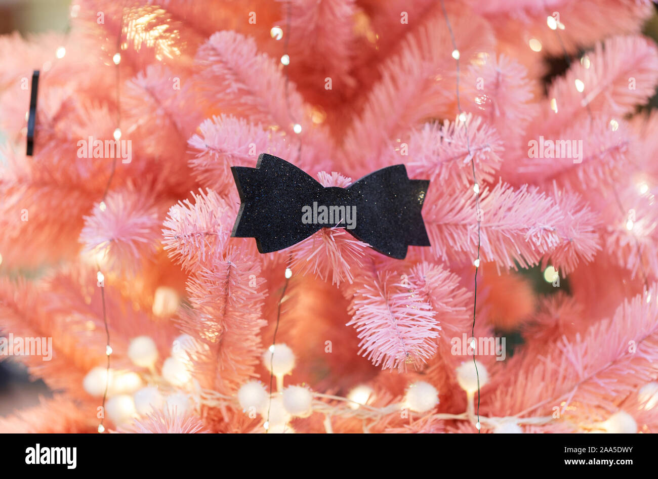 Pink christmas tree with festive lights and decor bow tie. Concept of Christmas background Stock Photo