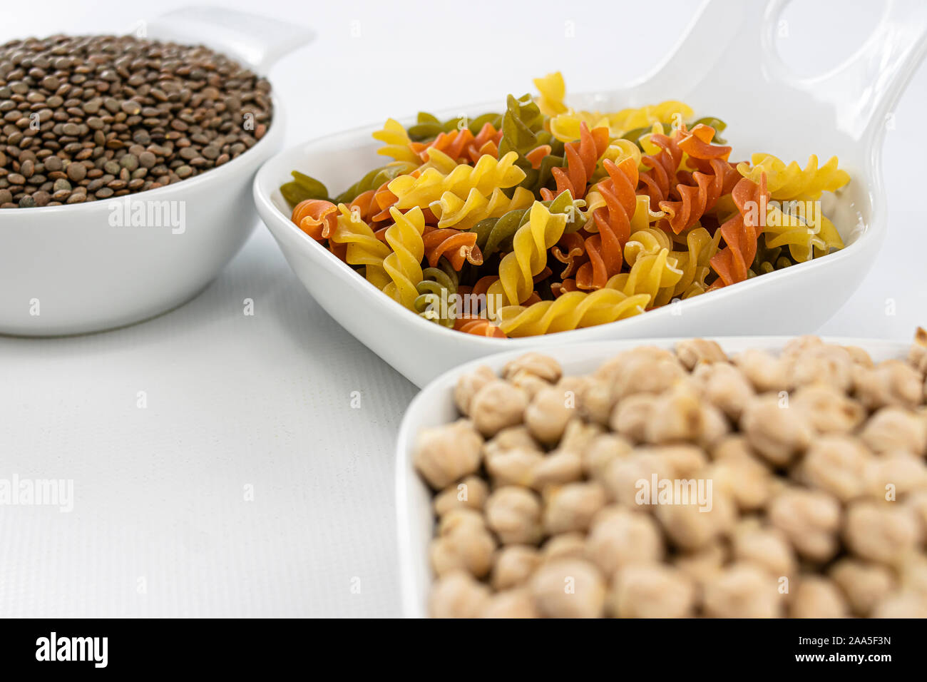 Close up view of colorful pasta, chickpeas and lentils in white bowls on white background Stock Photo