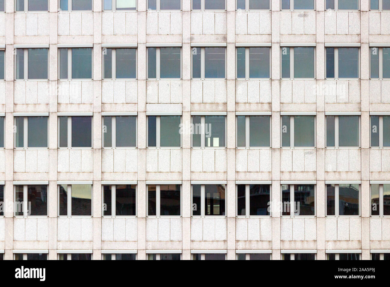 Gray facade of a multi storey office building with a symmetrical pattern of windows. Stock Photo